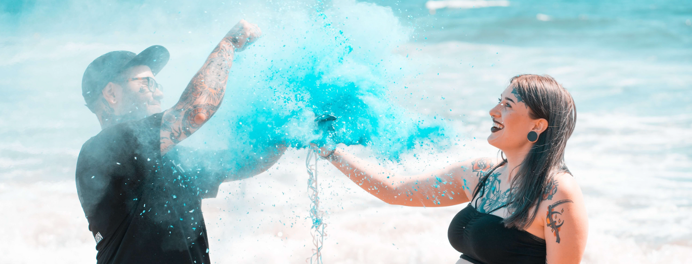 A couple doing a gender reveal on a beach popping a balloon full of colour powder