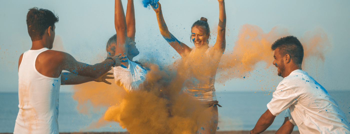 A group of people throwing colour powder in the air on a beach.