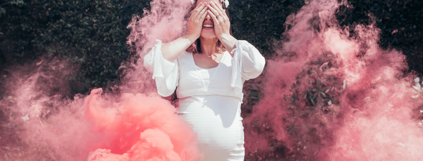 A pregnant woman surrounded by pink colour powder at a gender reveal