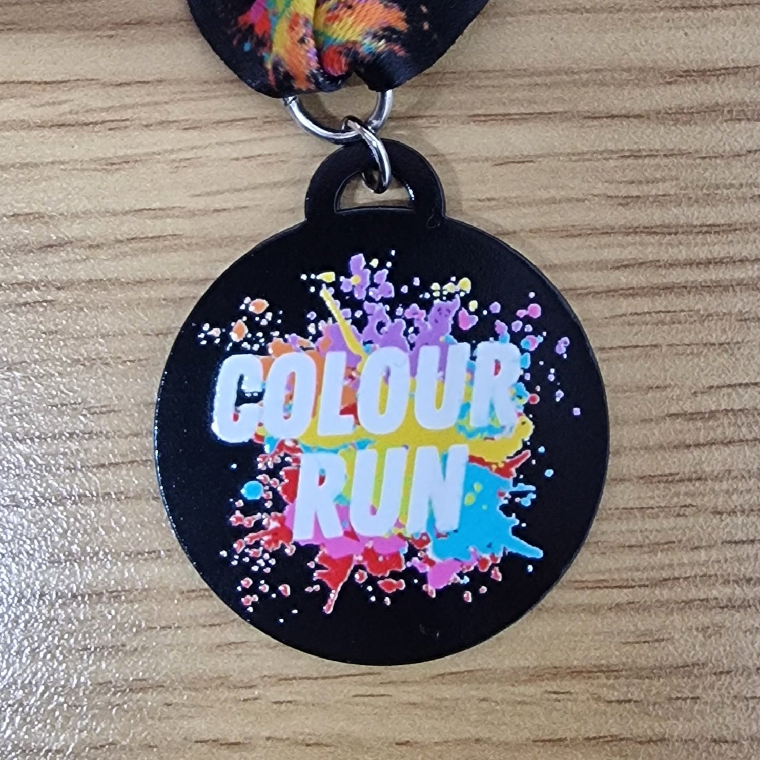 A round black medal with the text 'COLOUR RUN' in the center surrounded by a colorful paint splash design.