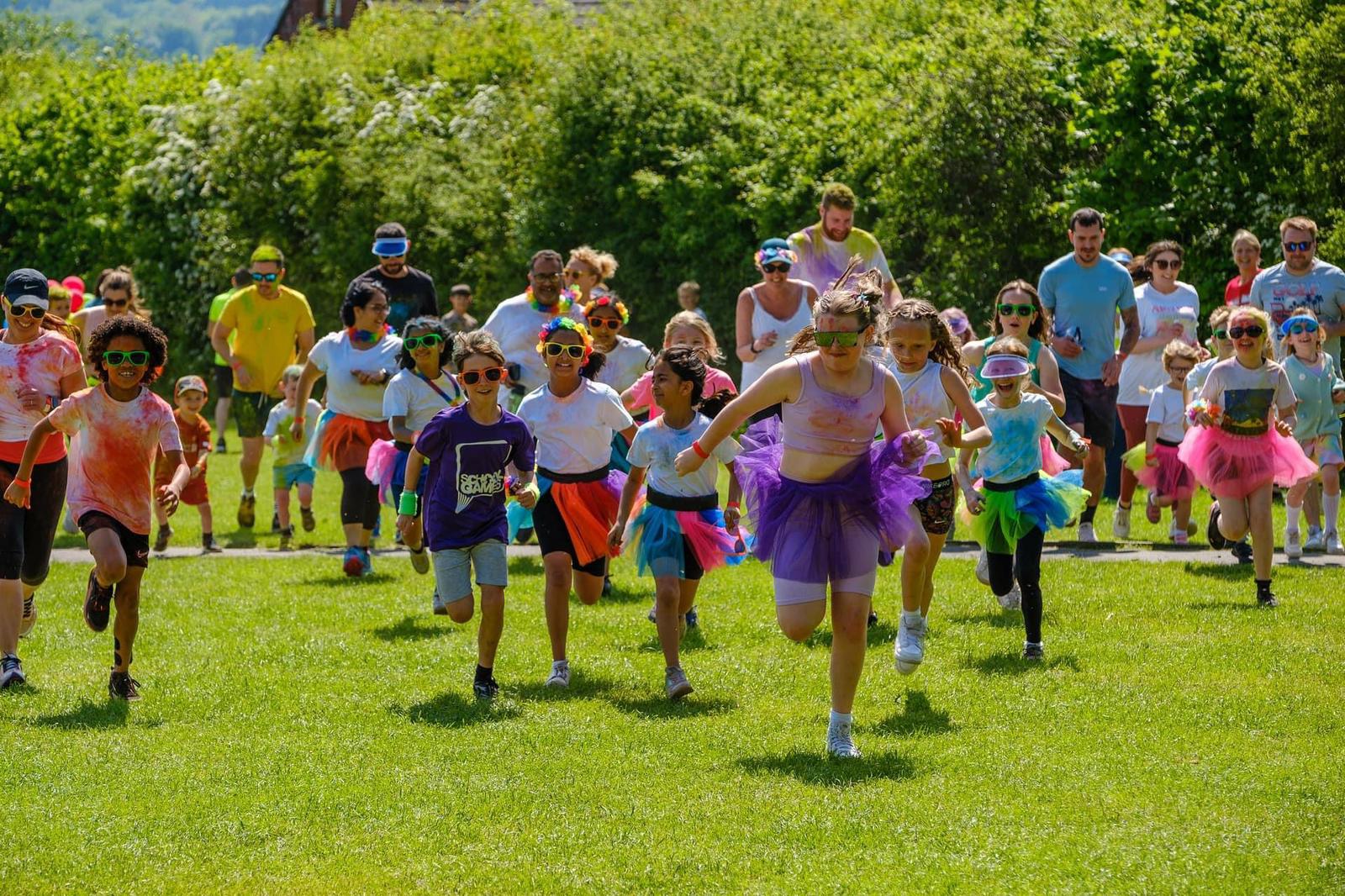Children dressed in colourful attire running in a field for a colour run fundraising event.