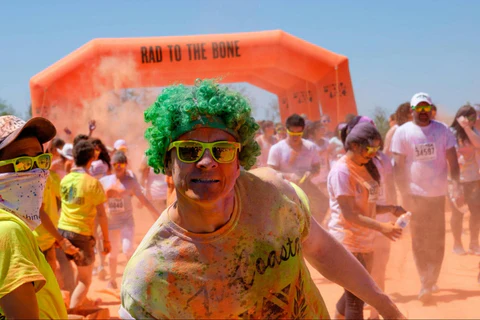 Person with green wig and sunglasses at a color run event with 'Rad to the Bone' inflatable arch in the background.