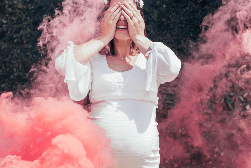 Person in a white dress standing amidst pink smoke