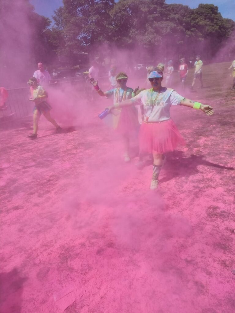 A pink cloud of colour powder is seen being walked through by rainbow run attendees