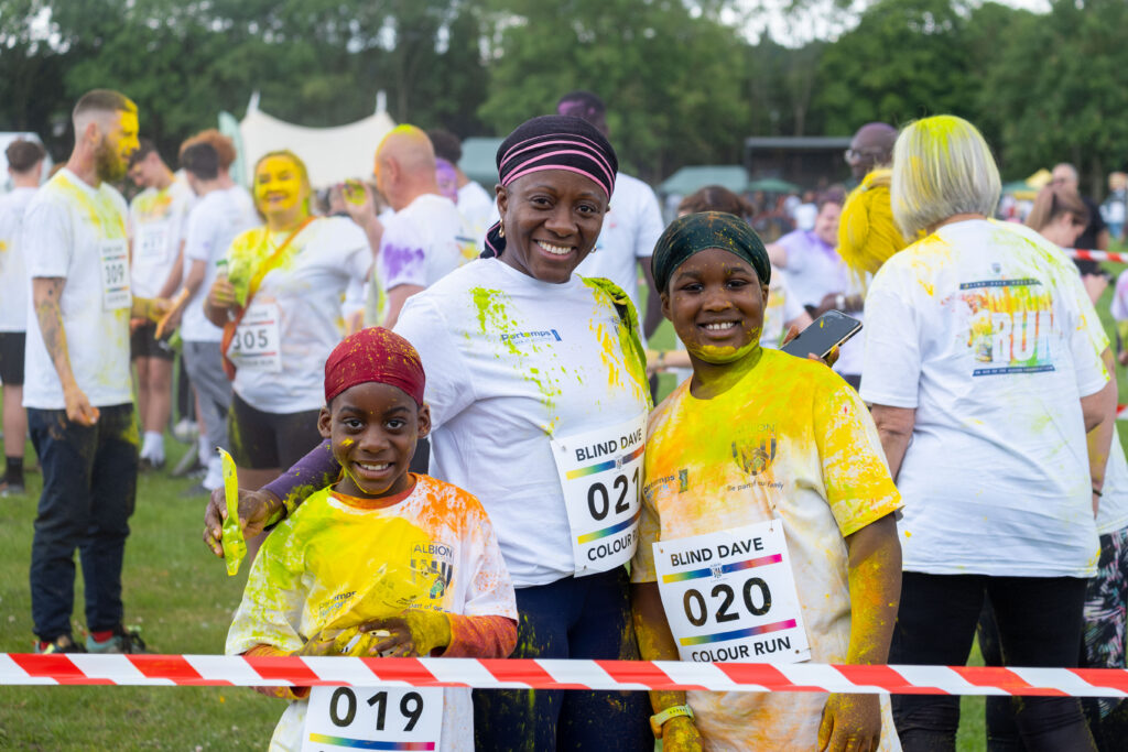 A family, covered in yellow powder, smiling at a rainbow run event.