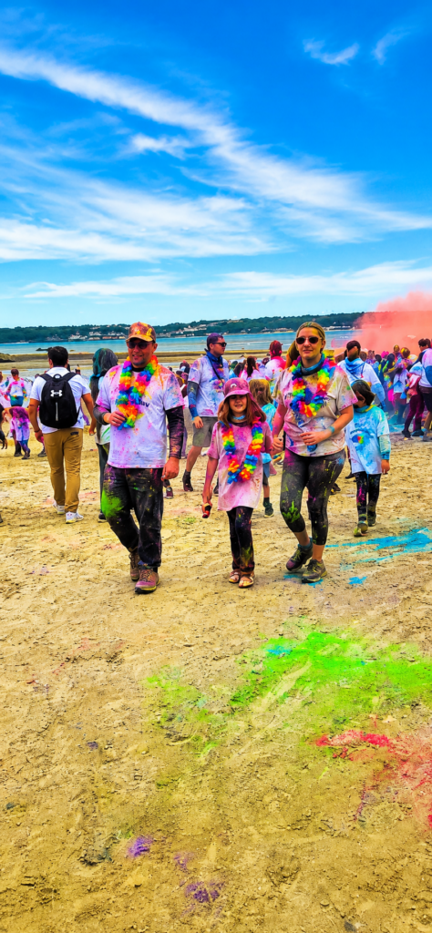 Family covered in colourful powder walking along West Park Beach